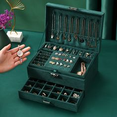 a woman's hand holding an open green jewelry box filled with necklaces and rings