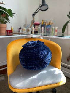 a blue crocheted pot sitting on top of a yellow chair in front of a desk