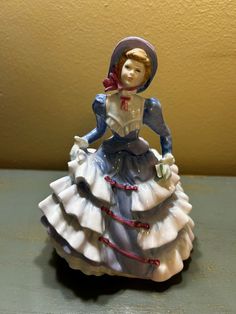 a ceramic figurine of a woman wearing a blue dress and hat with a red ribbon around her neck