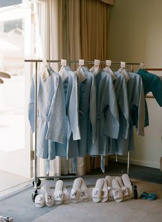 several pairs of shoes are on the floor next to a rack with shirts hanging from it