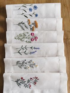 six embroidered napkins with flowers on them sitting on a wooden table next to each other