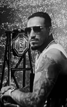 a man with tattoos and sunglasses standing in front of a wall