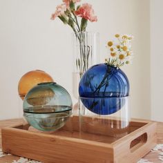 two vases with flowers in them sitting on a wooden tray next to each other