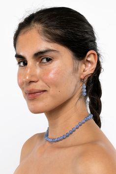 a woman wearing a necklace and earrings with blue beads on her neck, looking at the camera