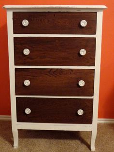 a white and brown dresser with knobs on the bottom drawer, against an orange wall