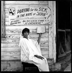 a black and white photo of a woman sitting in front of a store holding an open book