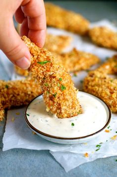 a person dipping something into a small white bowl filled with ranch dressing on top of some chicken nuggies