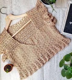 a crocheted sweater next to potted plants on a white tile floor with a wooden hanger