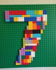 the letter c made out of legos on a green wall with white and yellow bricks