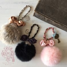 three pompom keychains on a table next to an old book and purse