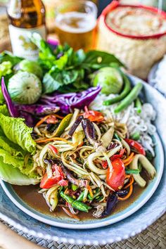 a plate filled with noodles and vegetables on top of a table next to some beer