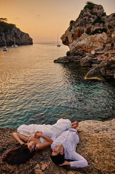 two people laying on rocks near the water