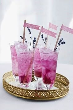 two glasses filled with pink drinks on top of a gold tray