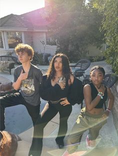 three young people posing for a photo in front of a house with their hands on their hips