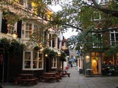 an empty street with tables and benches on the side walk in front of buildings that are lined with trees