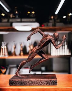 a bronze statue of a running man on a wooden table in a room with shelves