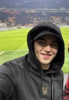 a man in a hoodie taking a selfie at a soccer game