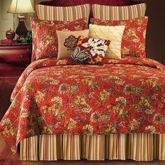 a red bed covered in lots of pillows next to a night stand with a lamp on it