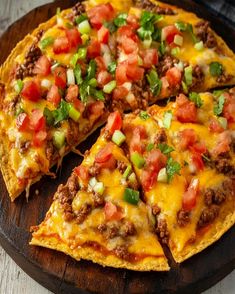 a pizza with cheese, meat and veggies cut into slices on a wooden platter