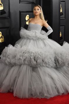 lady in grey gown standing on red carpet with gold awards around her neck and hands on hips