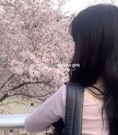 a woman with long black hair standing next to a tree