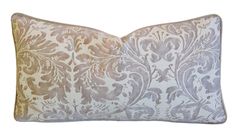 a white and grey pillow with an ornate design on the front, along with a gold border