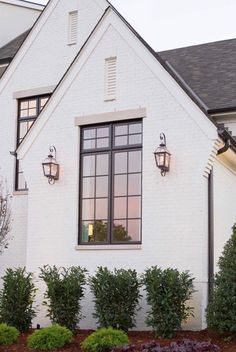 a white house with black windows and plants in the front yard, on a cloudy day