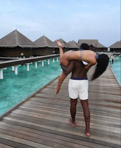 a man carrying a woman on his back while standing on a wooden pier over water