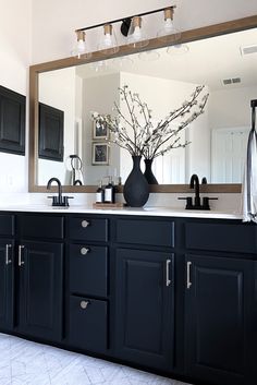 a bathroom with black cabinets and a large mirror on the wall above it is decorated with flowers in a vase