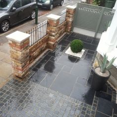 a black car is parked in front of a brick fence and gated area with potted plants