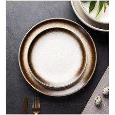 an empty plate on a table next to some forks and spoons with two speckled eggs