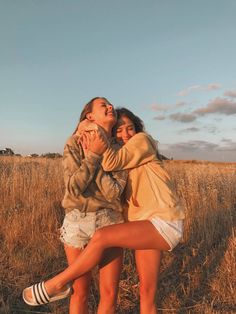 two young women are hugging in a field