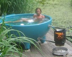 a woman in a large blue tub sitting on a wooden deck next to a pond