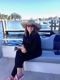 a woman wearing a hat and sunglasses sitting on a boat in front of the water