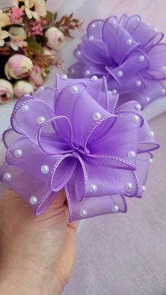 two purple flowers with pearls on them are being held up by someone's hand