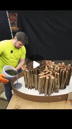 a man in yellow shirt standing next to a table filled with wooden logs and a cup