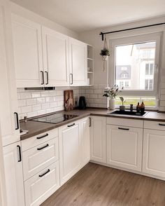 a kitchen with white cabinets and wood flooring in front of a large open window