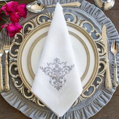 a silver and gold plate with a white napkin on it, next to pink flowers