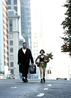 a man and woman walking down the street with flowers in their hands, carrying luggage