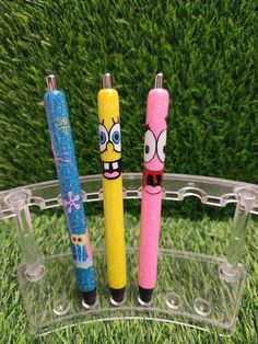 three pens with faces drawn on them sitting in the grass next to some fake grass