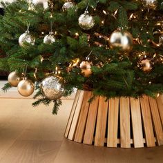 a christmas tree with gold and silver ornaments in a wooden basket on the floor next to a fireplace