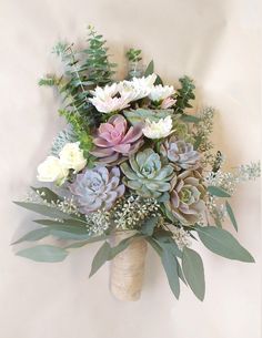 a bouquet of succulents and greenery is displayed on a white wall