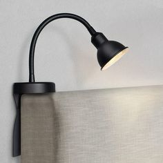 a black lamp on the side of a bed with a white headboard and sheets