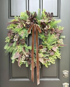 a wreath on the front door with pine cones and greenery