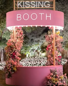 a pink sign that says kissing booth with flowers around it and lights on the sides