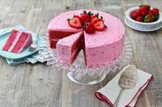 a pink cake with strawberries on top sits on a table next to plates and utensils