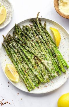 grilled asparagus on a white plate with lemons and seasoning next to it