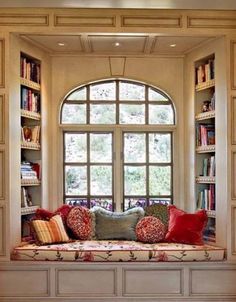 a window seat with pillows on it in front of a book shelf filled with books