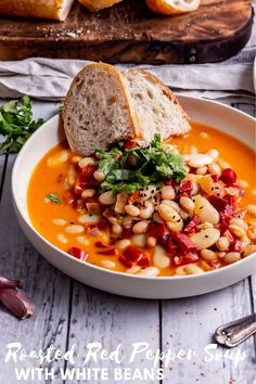 a white bowl filled with beans and bread on top of a wooden table next to sliced bread