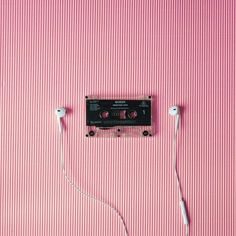 an old fashioned cassette player with ear buds plugged into the cord, on a pink striped background